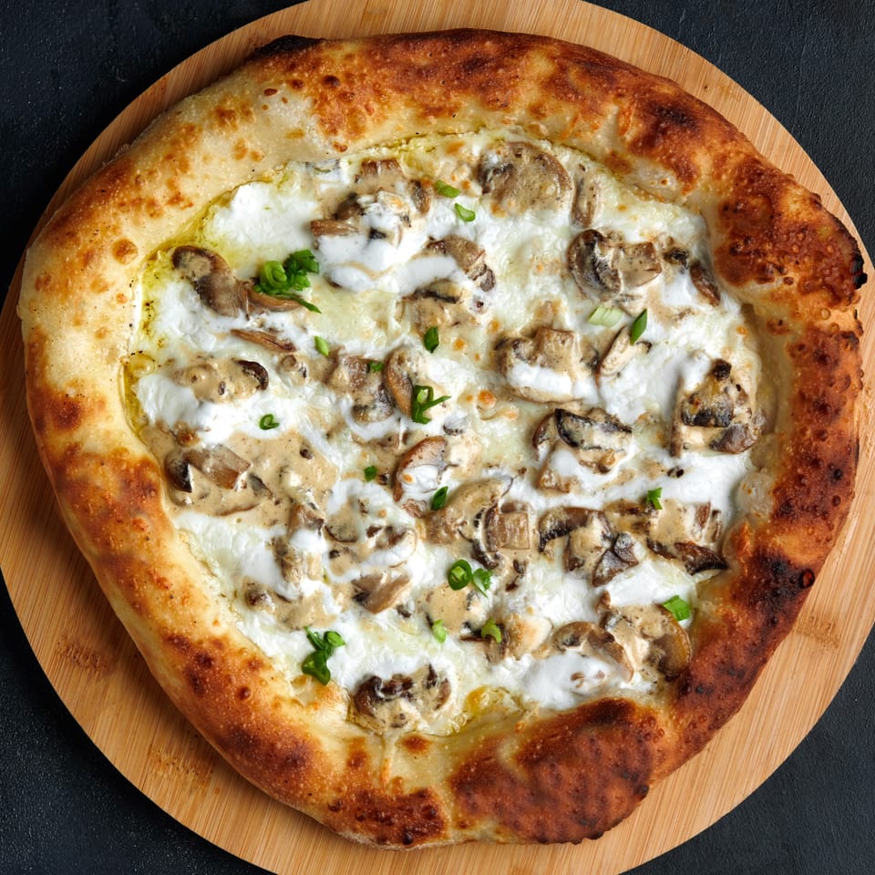Vincents' mushroom pizza with white sauce and green herbs on a wooden board.