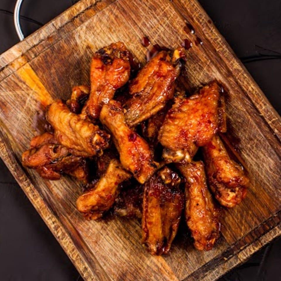 Glazed chicken wings on a rustic wooden cutting board, with dark sauce drizzled over them.